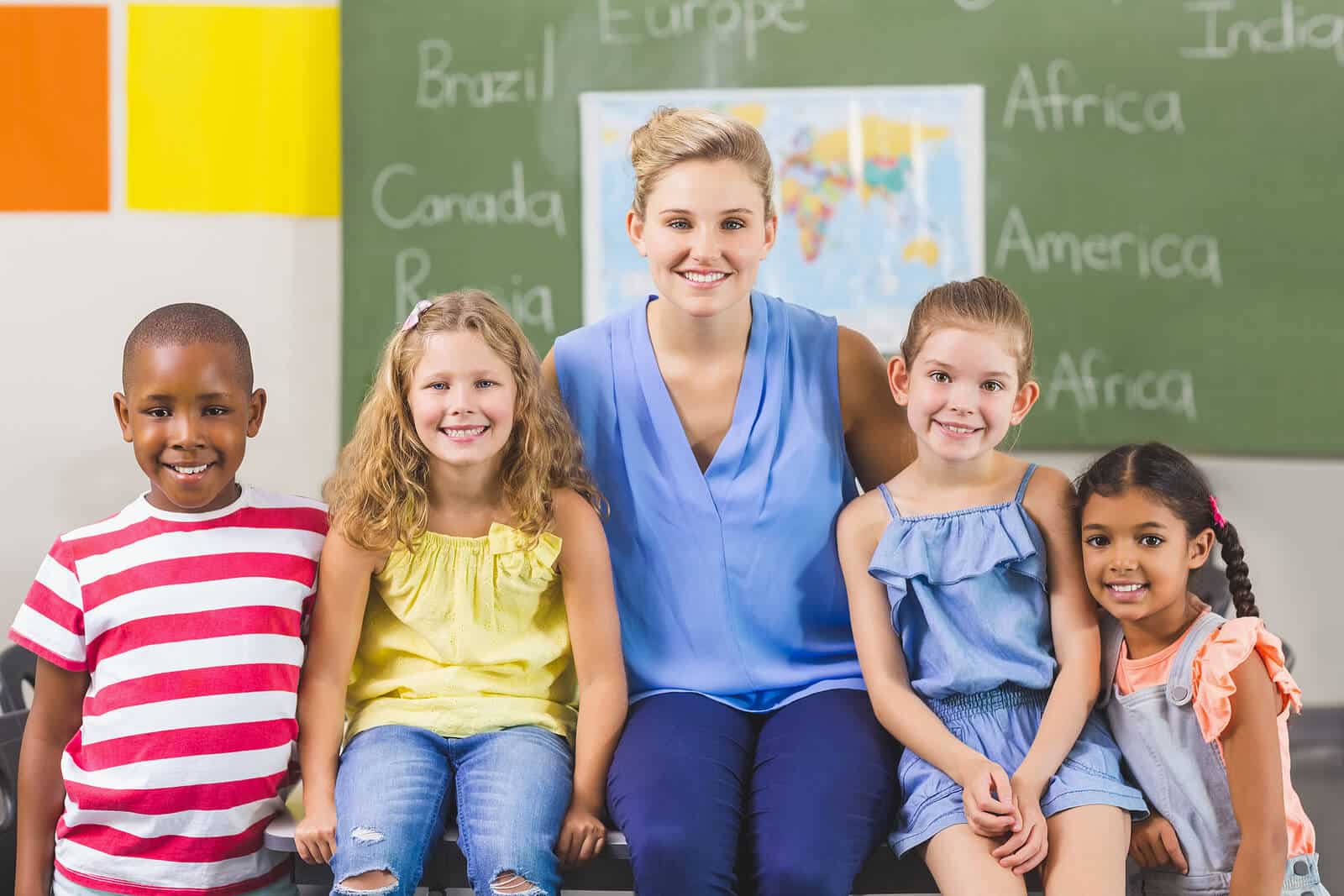 Lehrerin mit vier Schülern vor einer Tafel mit Landkarte