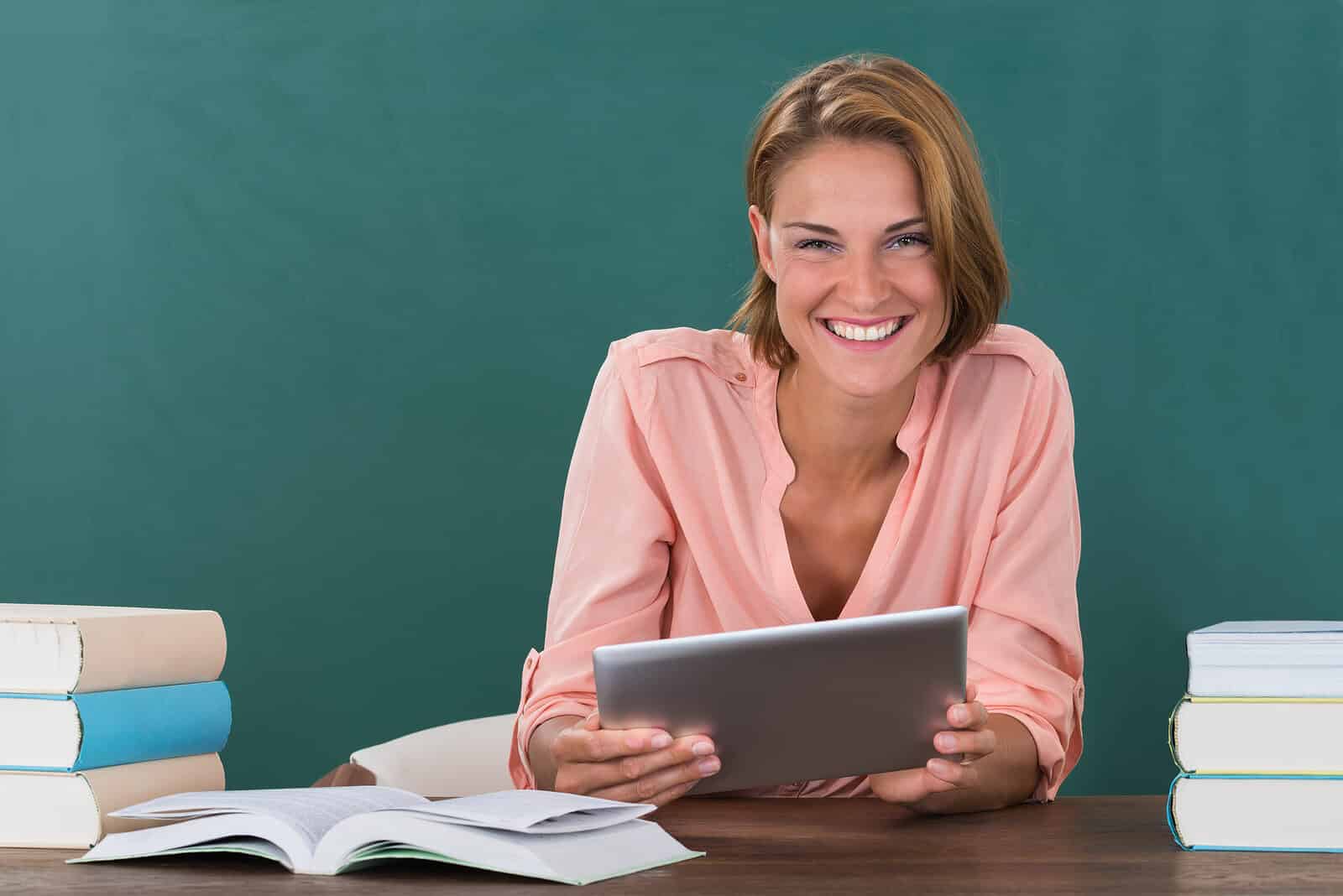Lehrerin mit Büchern und Tablet vor einer Tafel